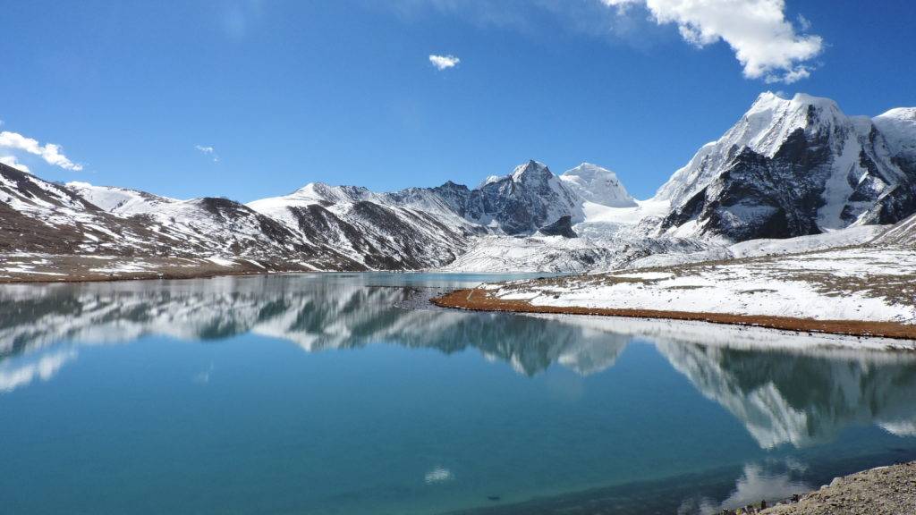 Reflection of mountains on the clear blue water of Gurudongmer lake under a clear blue sky