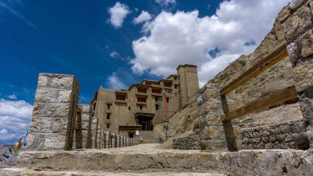 Leh Palace under a clear blue sky with white clouds floating around