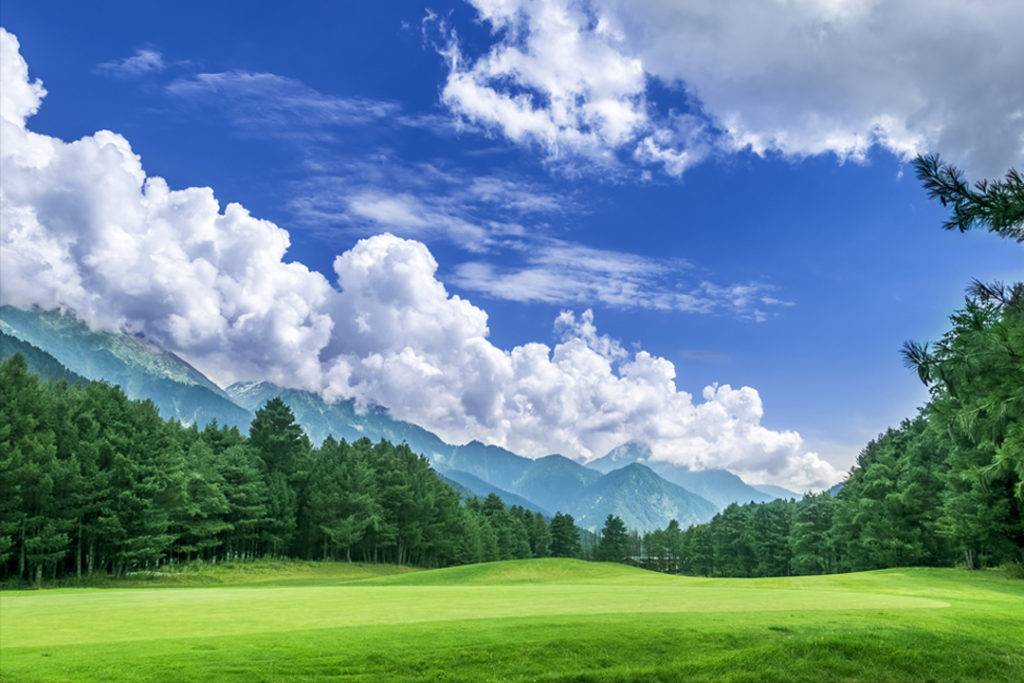 Pahalgam Golf Course surrounded by snow capped mountains, pine trees, lush green grass and the perfect blue sky with white clouds