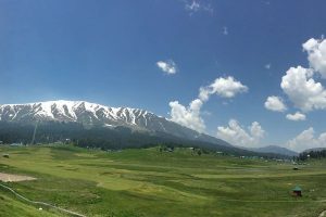 Green valleys of Gulmarg surrounded by snow capped mountains and a clear blue sky