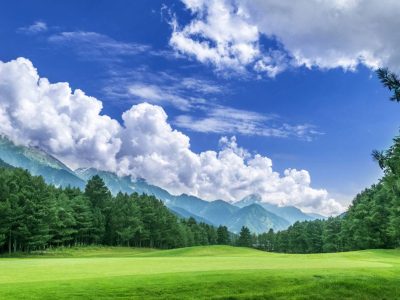 Pahalgam Golf Course surrounded by snow capped mountains, pine trees, lush green grass and the perfect blue sky with white clouds