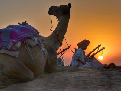 a camel and its owner taking rest in the desert during sunset